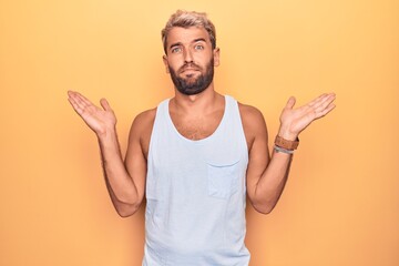 Poster - Young handsome blond man wearing casual sleeveless t-shirt over isolated yellow background clueless and confused with open arms, no idea and doubtful face.