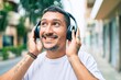 © Krakenimages.com - Young hispanic man smiling happy listening to music using headphones at street of city.