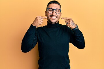 Poster - Handsome man with tattoos wearing turtleneck sweater and glasses smiling cheerful showing and pointing with fingers teeth and mouth. dental health concept.