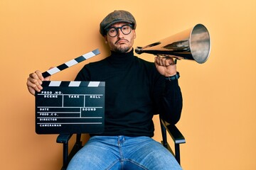 Poster - Handsome man with tattoos holding video film clapboard and louder depressed and worry for distress, crying angry and afraid. sad expression.