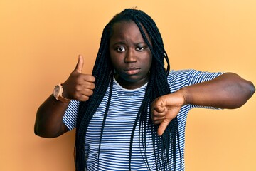 Poster - Young black woman with braids doing thumbs down and thumbs up gesture skeptic and nervous, frowning upset because of problem. negative person.