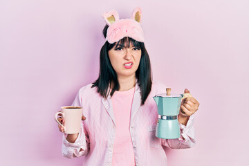 Poster - Young hispanic woman wearing sleep mask and robe drinking coffee clueless and confused expression. doubt concept.