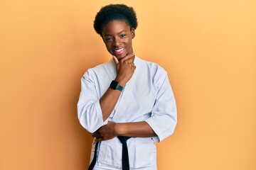 Canvas Print - Young african american girl wearing karate kimono and black belt looking confident at the camera smiling with crossed arms and hand raised on chin. thinking positive.