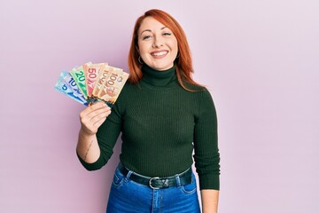 Sticker - Beautiful redhead woman holding canadian dollars looking positive and happy standing and smiling with a confident smile showing teeth