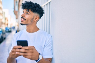 Young arab man smiling happy using smartphone leaning on the wall.