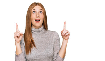 Young irish woman wearing casual clothes amazed and surprised looking up and pointing with fingers and raised arms.