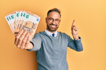 Sticker - Handsome middle age man holding bunch of euros smiling happy pointing with hand and finger to the side