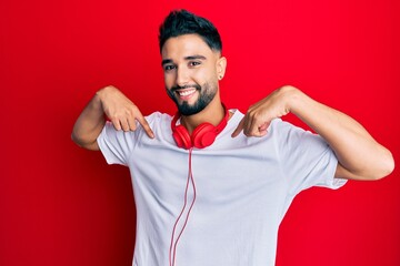 Poster - Young man with beard listening to music using headphones looking confident with smile on face, pointing oneself with fingers proud and happy.