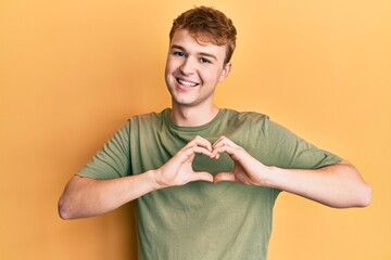 Young caucasian man wearing casual green t shirt smiling in love doing heart symbol shape with hands. romantic concept.