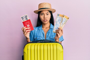 Poster - Young chinese woman holding boarding pass and passport in shock face, looking skeptical and sarcastic, surprised with open mouth