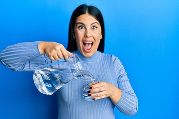 Sticker - Beautiful brunette woman pouring water in glass celebrating crazy and amazed for success with open eyes screaming excited.