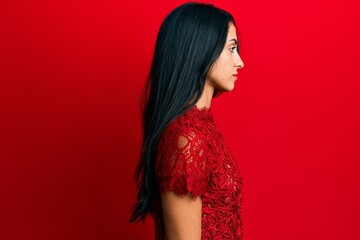 Wall Mural - Beautiful hispanic woman wearing elegant clothes over red background looking to side, relax profile pose with natural face with confident smile.