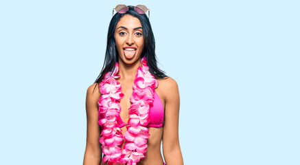 Wall Mural - Beautiful hispanic woman wearing bikini and hawaiian lei sticking tongue out happy with funny expression. emotion concept.