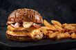 hamburguesa doble carne con tocineta queso y cebolla frita en un fondo negro  y al lado papas fritas 