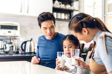 Portrait of enjoy happy love asian family father and mother with little asian girl smiling and having breakfast drinking and hold glasses of milk at table in kitchen