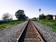 Railroad Track Along The Coast In Carpinteria, California With Palm Tree And American Flag At Half Mast In The Distance.