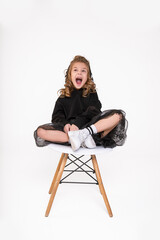 Funny little girl sit on fashionable chair on white background in studio and loudly yelling or laugh. Baby emotion concept