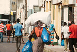 Fototapeta  - Inhambane, Mozambique, September, 19th 2018: African woman carrying large packages on a street full of men.