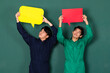 © Bangkok Click Studio - portrait of two young confident handsome Asian men wearing colorful mechanic jumpsuits standing smiling holding a yellow and red text speech bubble over green background