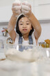 © Bangkok Click Studio - A little cute Asian girl, 7 years old, learning how to make bread and bakery, she tries to mix flour and spread it in the air with a curious and happy smiley face in a modern kitchen.