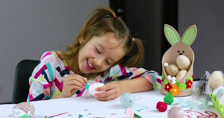 happy little girl painting, drawing with brush eggs at home.