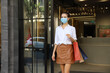 © torsakh - Beautiful lady woman wear face mask walking out from the door glasses of shopping mall and feeling cheerful posing and happy holiday sale, new normal or covid-19 pandemic protection