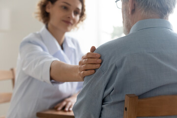 Close up of supportive female doctor touch comfort upset elderly male patient at consultation in clinic. Caring woman nurse or GP caress support mature man at meeting in hospital. Geriatric concept.