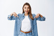 © Cookie Studio - Excited blond woman checking out awesome news, pointing fingers down and staring amazed, showing advertisement on bottom copy space, standing against white background