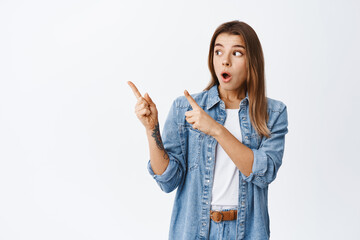 Wall Mural - Young impressed woman with blond hair, drop jaw and gasping amazed while pointing at upper left corner, checking out advertisement on copy space, white background