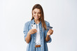 © Cookie Studio - Online shopping. Portrait of smiling blond woman paying with plastic credit card on smartphone app, standing with mobile phone and bank card against white background