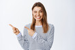 © Cookie Studio - Cheerful smiling woman inviting to check out promo, pointing fingers left and looking happy, winking at camera to motivate you, white background