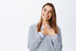 © Cookie Studio - Portrait of blond smiling woman holding hands on heart, looking with thankful face, express gratitude and delight, appreciate help, white background