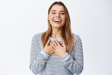 Wall Mural - Image of beautiful blond woman laughing, having fun and chuckling, holding hands on chest with gratitude, thanking you, standing over white background