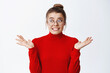 © Cookie Studio - Oops what to I do now. Nervous young woman in glasses worried as making mistake, shrugging and looking aside indecisive, know nothing, cant understand, white background