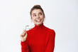 Portrait of smiling happy woman thinking, looking up and holding glasses in hands, imaging something, having interesting thought, standing against white background