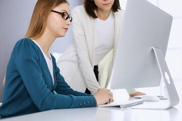 Businesswoman giving presentation to her female colleague while they sitting at the desk with computer. Group of business people working in office. Teamwork concept