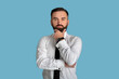 © Prostock-studio - Portrait of pensive young businessman in white shirt and tie thinking over something on blue studio background