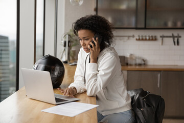 Wall Mural - Confident African American businesswoman making phone call, using laptop, searching information, consulting client, negotiating with business partner, sitting at table with motorcycle helmet