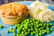 Homemade pastry meat pie and mash potatoes with green peas on a turquoise plate