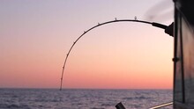 Silhouette Of Person Catching A Big Fish. Person Catching Big Fish On Boat During Sunset. Sunset On Boat. Man Reeling In Big Fish On Boat In The Ocean