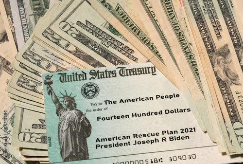 Stack of 20 dollar bills with US Treasury illustrative check to illustrate American Rescue Plan Act of 2021 payment on cash background © steheap