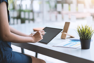 Close-up of a woman hand using a tablet and document placed on a modern office desk.