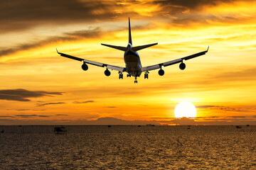 Wall Mural - rear image commercial passenger aircraft or cargo transportation airplane fly over coast of sea after takeoff from airport in evening with sun and golden sunset seascape view