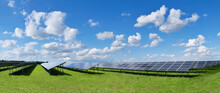 Solar Power Plant, Blue Solar Panels On Orange Autumn Grass Field Under Blue Sky With Clouds. Toned Panoramic Image. Solar Power Generation, Renewable Energy Production