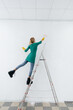 © Andrii - A young girl on a stepladder paints a white wall with a roller. Repair of the interior.