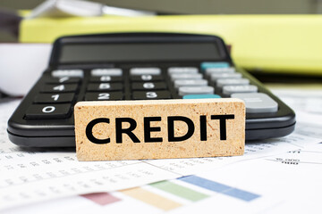 The word credit is written on a wooden cube that stands on financial documents against the background of a black calculator. Business and financial concept