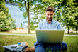 © baranq - smiling young businessman working on laptop having lunch in the park