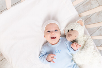 Wall Mural - baby in the crib, portrait of a smiling baby 3 months in the crib with a teddy bear toy, children and birth concept