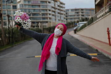 Girl in pink scarf and white mask with daisies outdoors. Cancer awareness concept. 