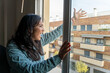 © Manuel - Adult woman looking out the window at home and shouting at her neighbor .